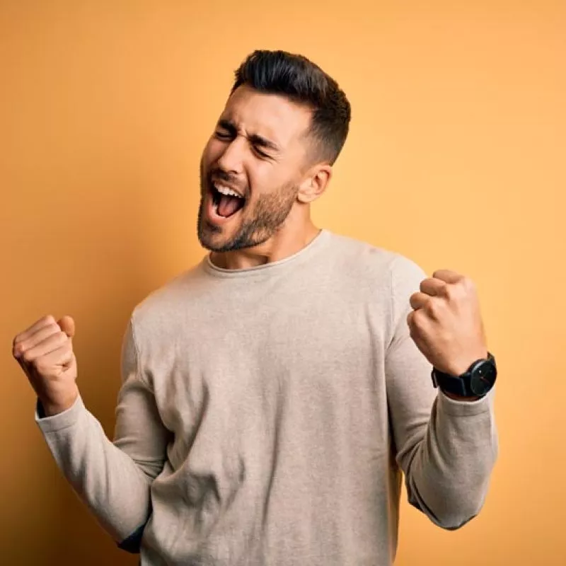 Young handsome man wearing casual sweater standing over isolated yellow background very happy and excited doing winner gesture with arms raised, smiling and screaming for success. Celebration concept.