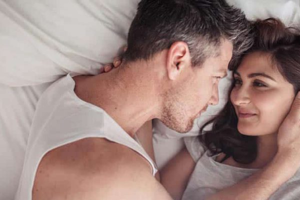 Overhead close up of young couple lying in bed together. Romantic couple in love looking at each other.